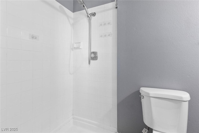 bathroom with a tile shower and toilet