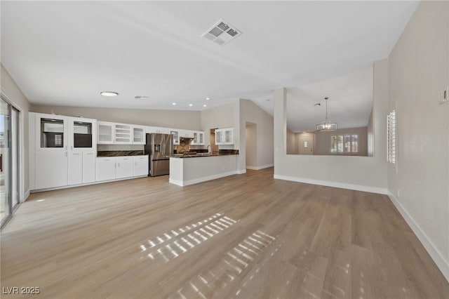 unfurnished living room featuring vaulted ceiling, a healthy amount of sunlight, an inviting chandelier, and light wood-type flooring