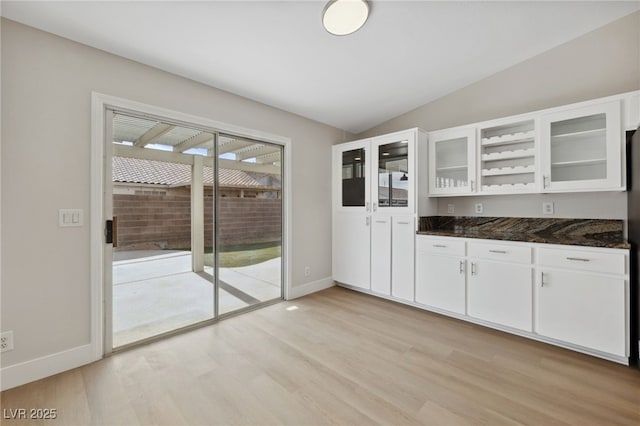 kitchen featuring dark stone countertops, light hardwood / wood-style flooring, lofted ceiling, and white cabinets