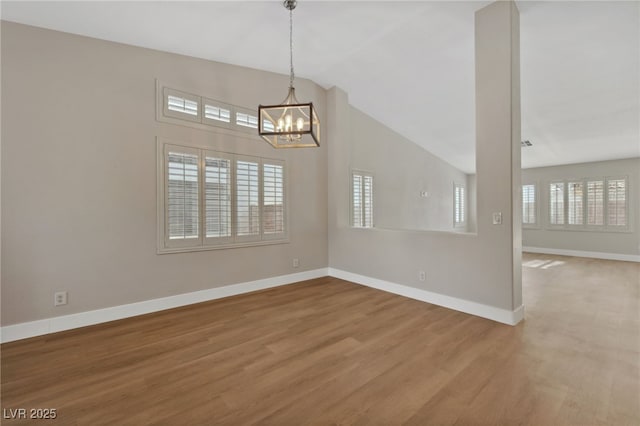 empty room featuring lofted ceiling, hardwood / wood-style floors, and a notable chandelier