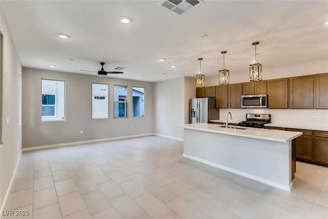 kitchen featuring sink, decorative light fixtures, ceiling fan, stainless steel appliances, and a kitchen island with sink