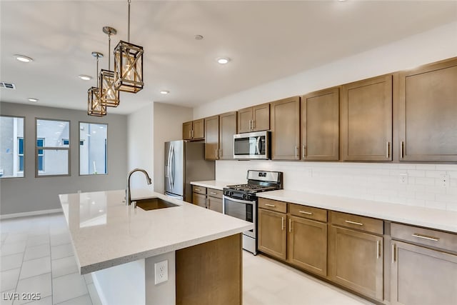 kitchen with pendant lighting, sink, a kitchen island with sink, stainless steel appliances, and light stone countertops