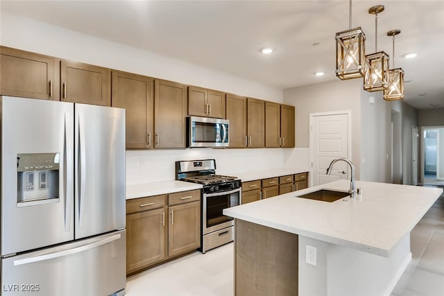 kitchen featuring sink, stainless steel appliances, light stone countertops, an island with sink, and decorative light fixtures