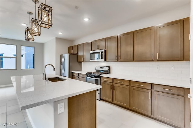 kitchen with tasteful backsplash, sink, a kitchen island with sink, light stone counters, and stainless steel appliances