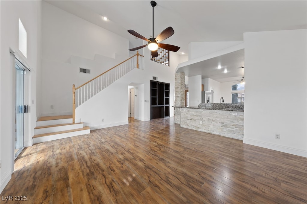 unfurnished living room featuring a high ceiling, ceiling fan, a wealth of natural light, and dark hardwood / wood-style flooring