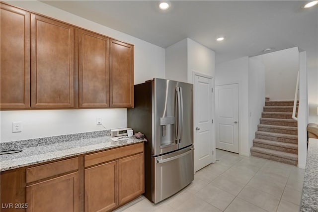 kitchen with light tile patterned flooring, stainless steel fridge, and light stone counters