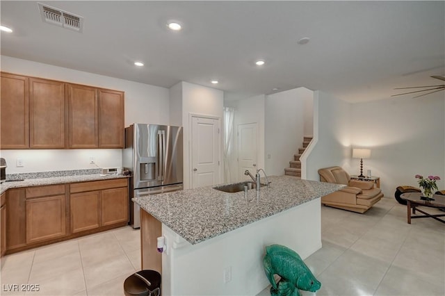 kitchen featuring stainless steel refrigerator with ice dispenser, light tile patterned flooring, sink, light stone counters, and a center island with sink