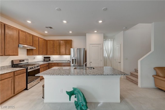 kitchen with light stone counters, sink, a center island with sink, and appliances with stainless steel finishes