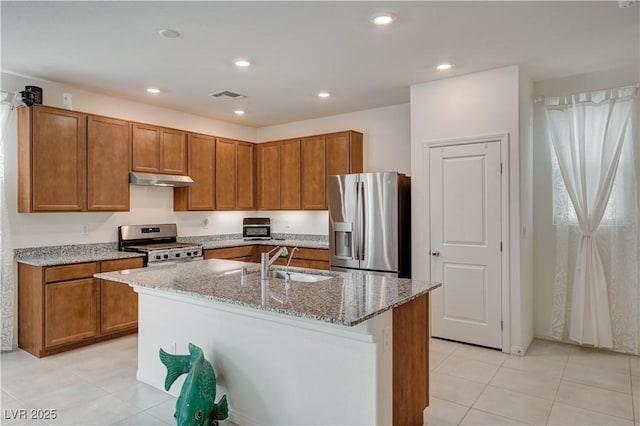 kitchen with light tile patterned flooring, sink, a kitchen island with sink, stainless steel appliances, and light stone countertops