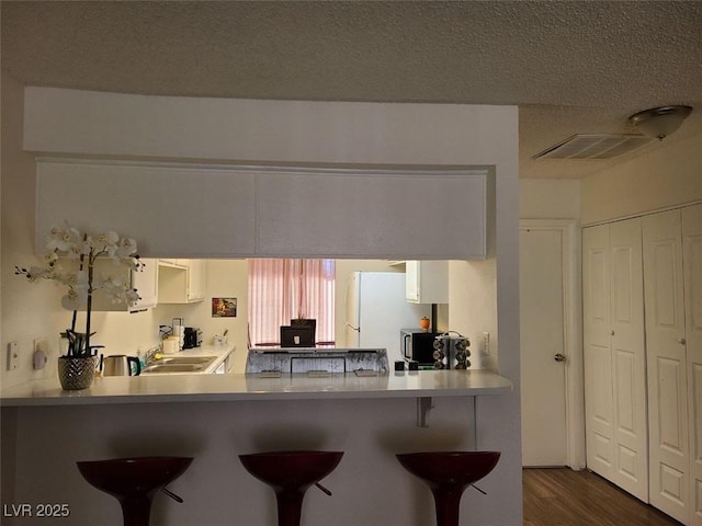 kitchen featuring a breakfast bar area, white cabinets, white fridge, kitchen peninsula, and a textured ceiling