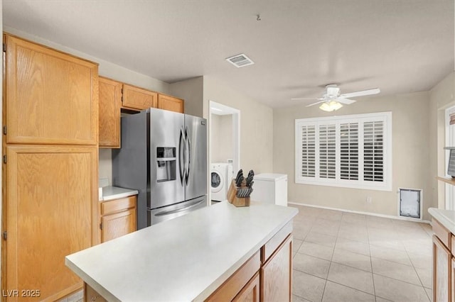 kitchen with light tile patterned flooring, stainless steel fridge with ice dispenser, light brown cabinets, ceiling fan, and washer / clothes dryer