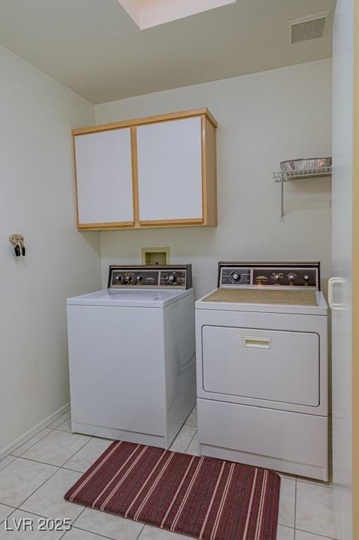 clothes washing area with visible vents, light tile patterned floors, washing machine and dryer, and cabinet space