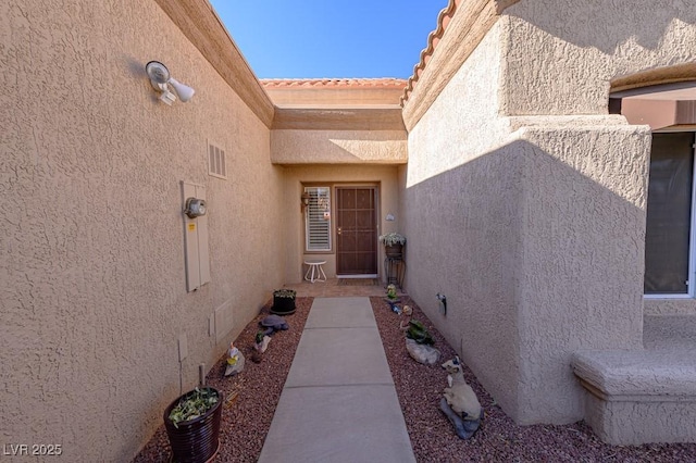 view of exterior entry with a tile roof and stucco siding