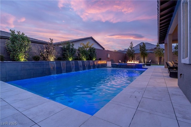 pool at dusk featuring pool water feature and a patio