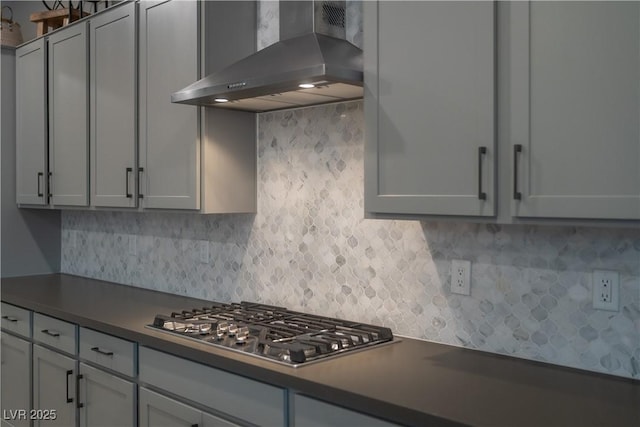 kitchen featuring wall chimney range hood, decorative backsplash, gray cabinets, and stainless steel gas cooktop