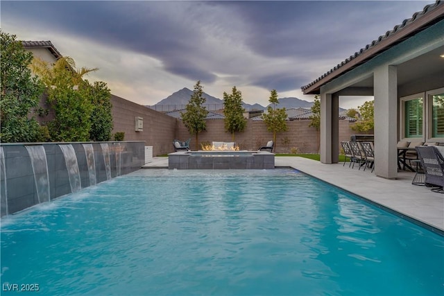 pool at dusk with a patio, pool water feature, and an in ground hot tub