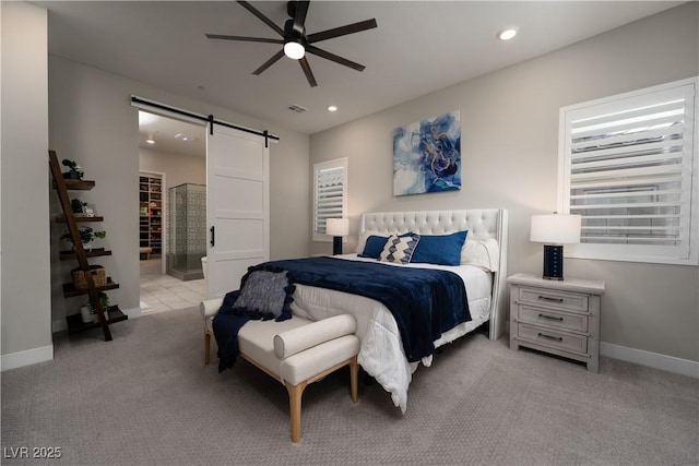 bedroom featuring ceiling fan, a barn door, light colored carpet, and ensuite bath