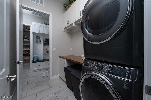 laundry area featuring light tile patterned flooring, cabinets, and stacked washer and dryer