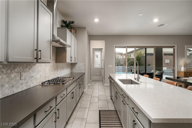 kitchen featuring sink, gray cabinets, a kitchen island with sink, backsplash, and stainless steel gas cooktop