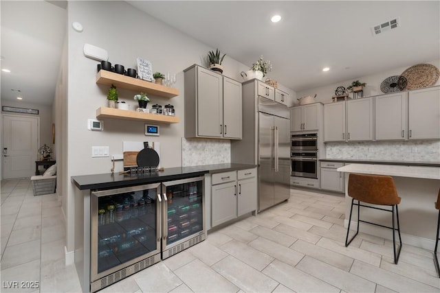 kitchen featuring a breakfast bar, gray cabinetry, wine cooler, decorative backsplash, and stainless steel appliances