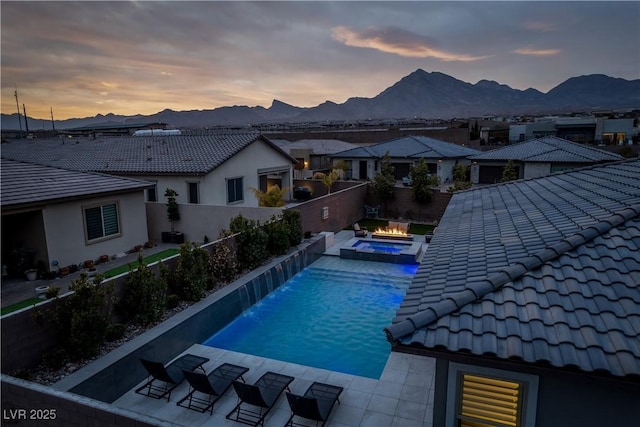 pool at dusk featuring an in ground hot tub, pool water feature, and a mountain view