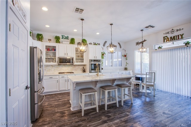 kitchen with white cabinetry, hanging light fixtures, a kitchen island with sink, stainless steel appliances, and dark wood-type flooring