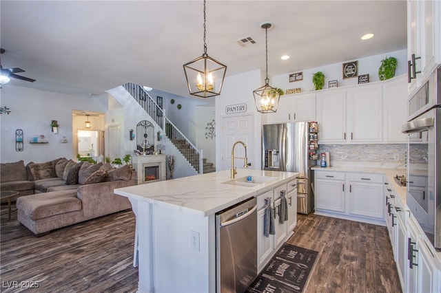 kitchen with decorative light fixtures, an island with sink, sink, white cabinets, and stainless steel appliances