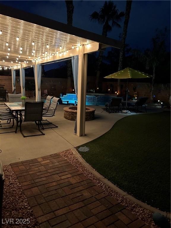 patio at night featuring a swimming pool and a fire pit