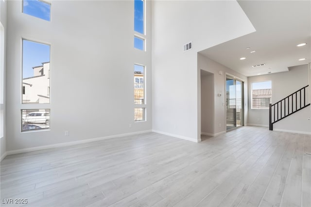 unfurnished living room featuring a high ceiling, plenty of natural light, and light hardwood / wood-style flooring