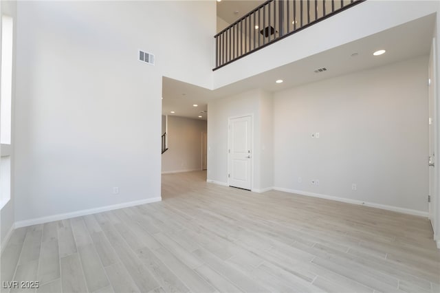 empty room featuring a towering ceiling and light hardwood / wood-style flooring