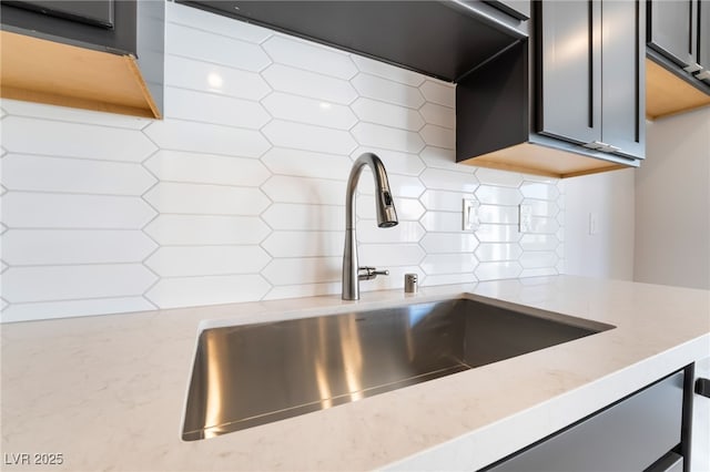 room details featuring light stone counters, gray cabinetry, sink, and backsplash