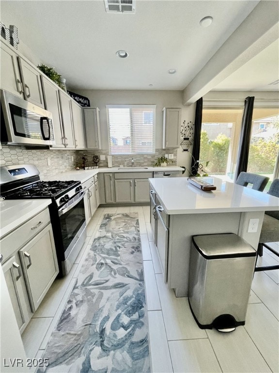 kitchen featuring a kitchen bar, gray cabinetry, a center island, appliances with stainless steel finishes, and decorative backsplash