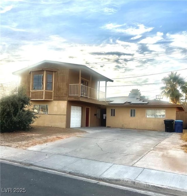 view of front facade featuring concrete driveway, a balcony, an attached garage, and stucco siding