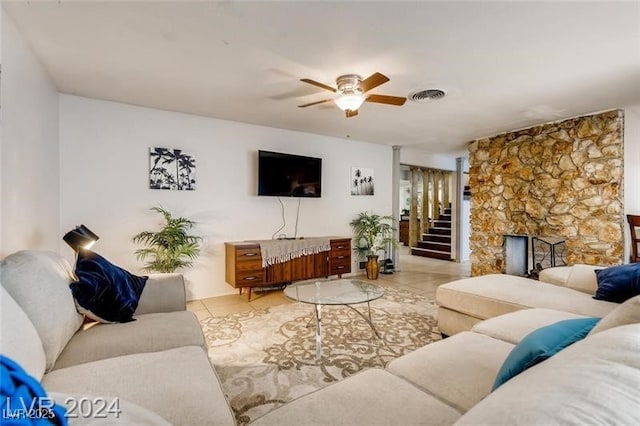 living room featuring light tile patterned flooring, ceiling fan, and a stone fireplace