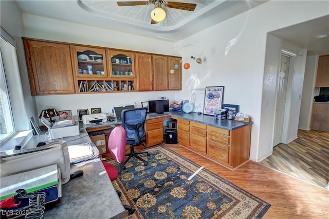 office space featuring ceiling fan, built in desk, light hardwood / wood-style floors, and a tray ceiling