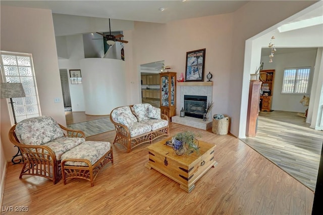 living room with a tiled fireplace, high vaulted ceiling, ceiling fan, and light wood-type flooring