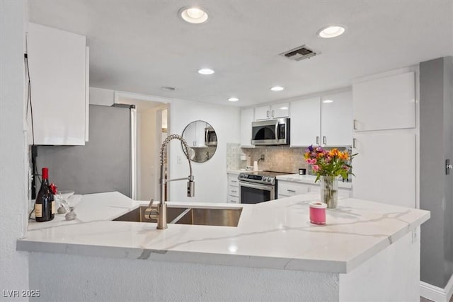 kitchen featuring sink, white cabinetry, light stone counters, appliances with stainless steel finishes, and kitchen peninsula