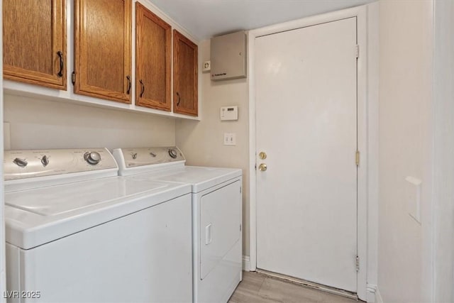 clothes washing area featuring cabinets, washing machine and clothes dryer, and light wood-type flooring