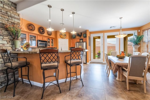 kitchen with visible vents, glass insert cabinets, brown cabinets, freestanding refrigerator, and a peninsula