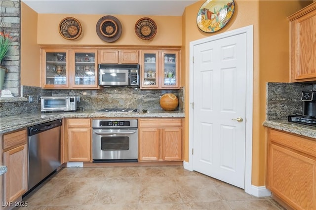 kitchen with a toaster, appliances with stainless steel finishes, light stone countertops, and decorative backsplash