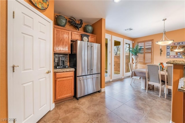 kitchen with light tile patterned floors, visible vents, brown cabinetry, freestanding refrigerator, and hanging light fixtures