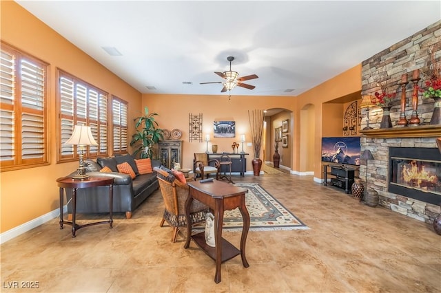 living area featuring arched walkways, a fireplace, a ceiling fan, and baseboards