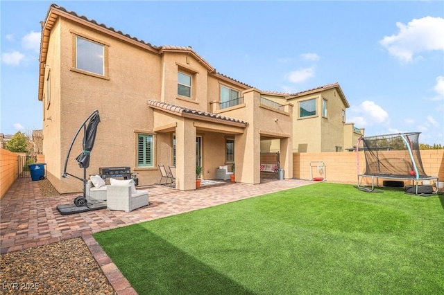 back of house with a trampoline, a patio area, and a lawn