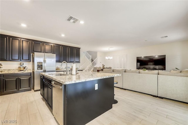 kitchen with sink, light hardwood / wood-style flooring, a kitchen island with sink, stainless steel appliances, and a notable chandelier