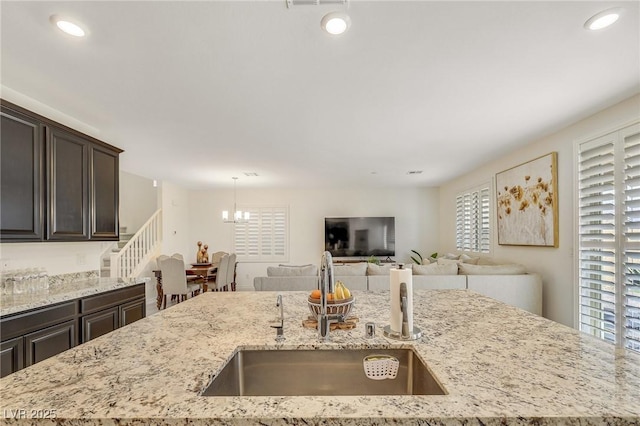 kitchen with sink, dark brown cabinetry, light stone countertops, a center island with sink, and decorative light fixtures