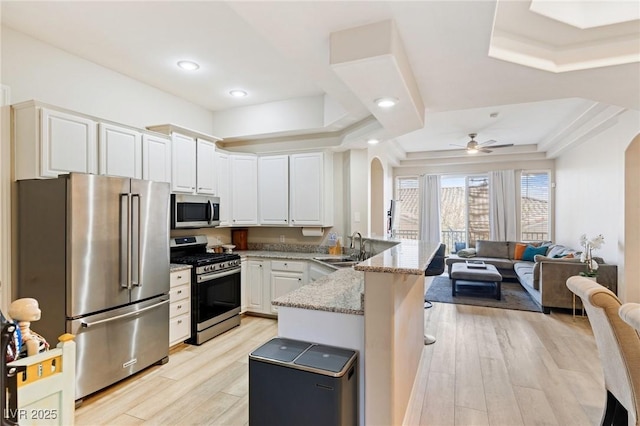 kitchen with white cabinetry, sink, kitchen peninsula, stainless steel appliances, and light stone countertops