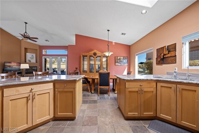 kitchen featuring decorative light fixtures, vaulted ceiling, light stone countertops, and a healthy amount of sunlight