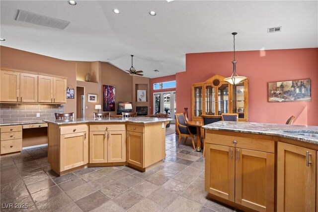 kitchen featuring pendant lighting, light brown cabinetry, and a kitchen island with sink