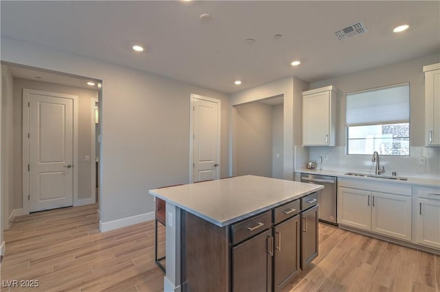 kitchen featuring sink, light wood-type flooring, stainless steel dishwasher, a kitchen island, and white cabinets