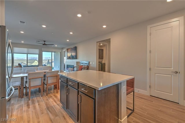 kitchen featuring a center island, dark brown cabinets, stainless steel refrigerator, ceiling fan, and light hardwood / wood-style floors